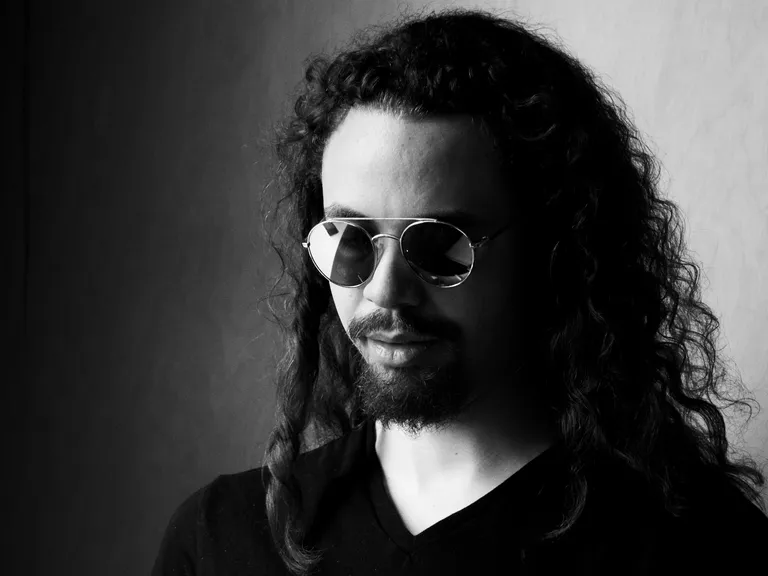 Black and white portrait of Tyler Taylor, late 20s, long dark hair, goatee, aviator sunglasses wearing a black vneck shirt.